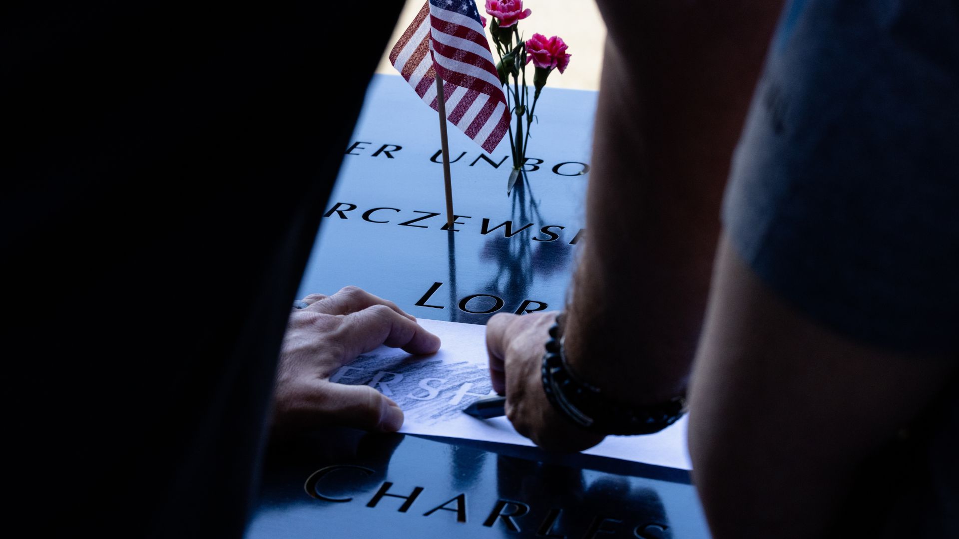 Hands holding paper as they make an imprint of a name on the Memorial parapet.