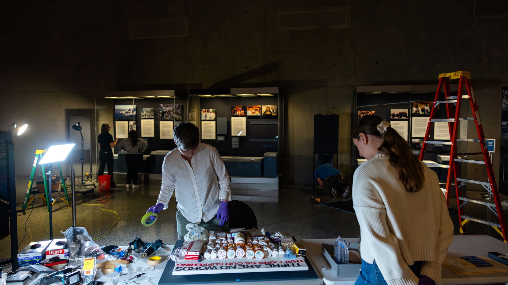 In a darkened room, museum staff members inspect a table of artifacts. 