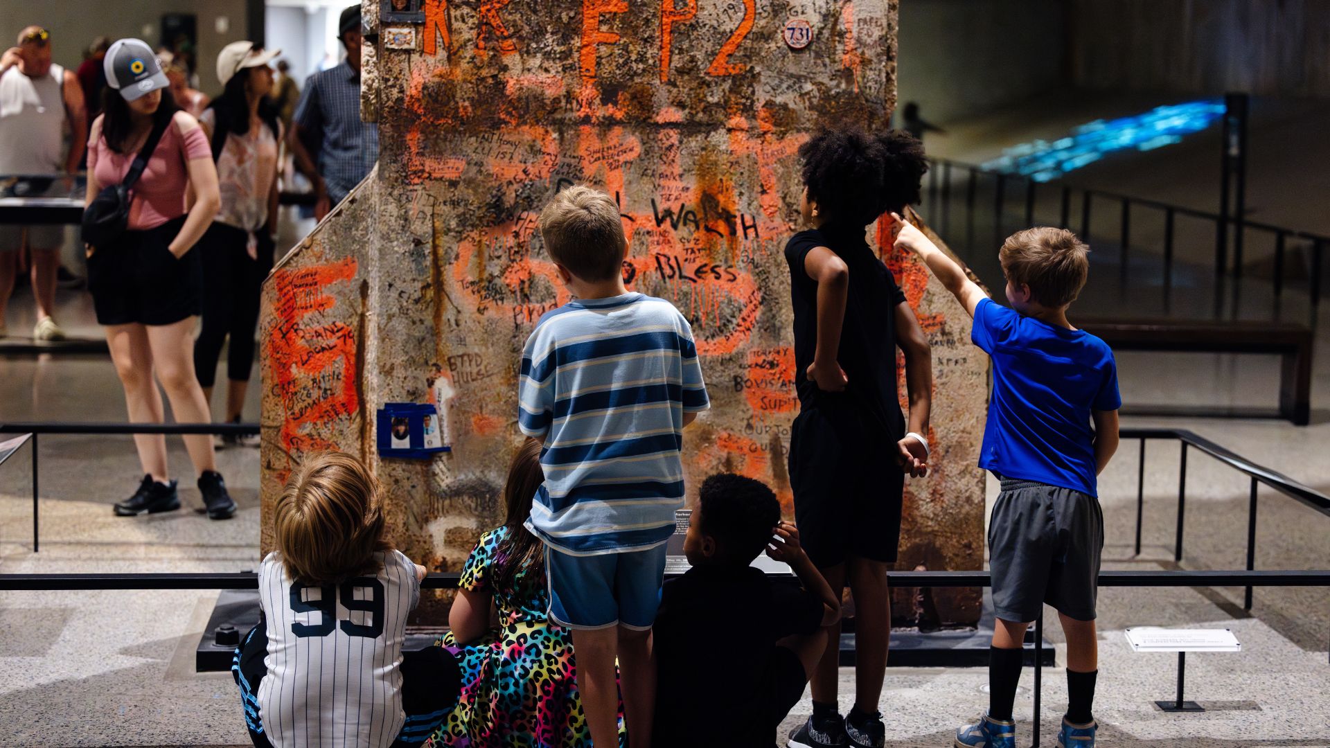 Back view of children looking at the Last Column, which is covered in hand painted messages and memorial artifacts.