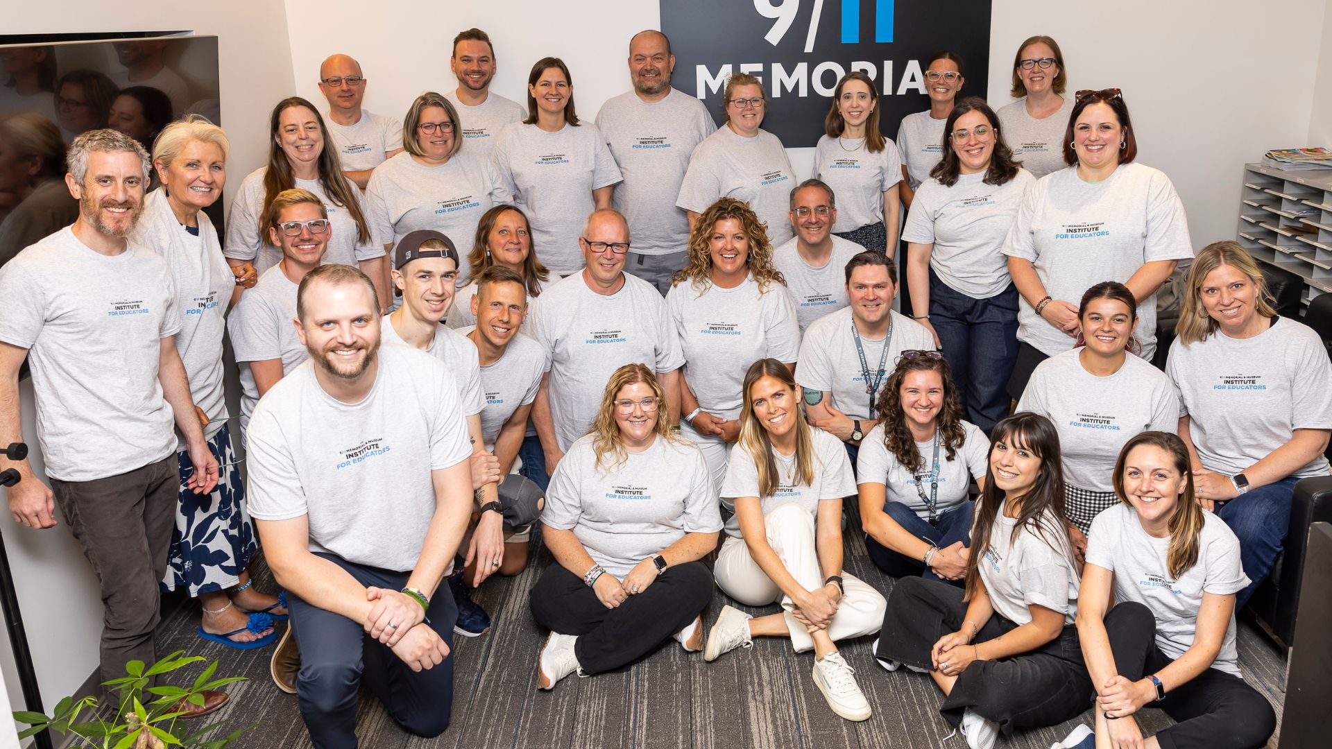 A group of smiling educators wearing matching white t-shirts pose informally in a conference room together.