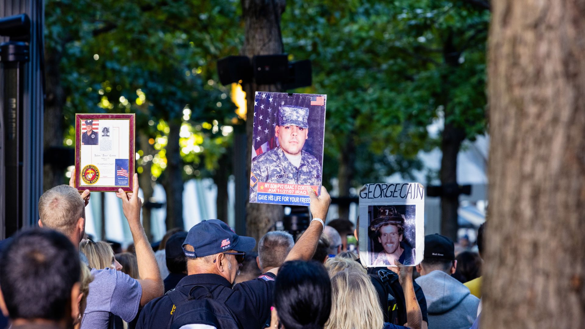 Back view of 9/11 commemoration ceremony participants as they hold up photographs and artifacts belonging to victims. 