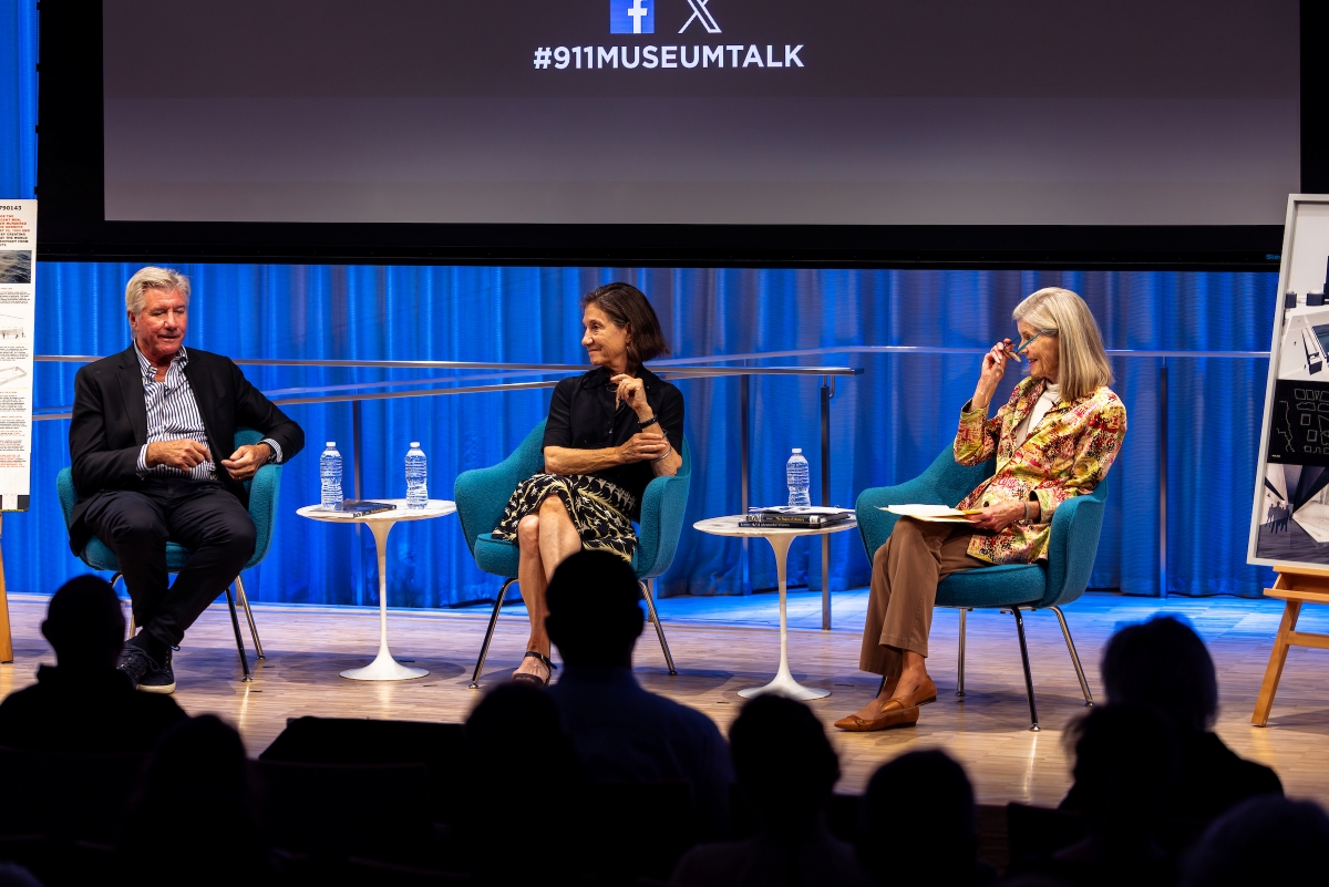 Three people sit on stage and talk together, smiling.