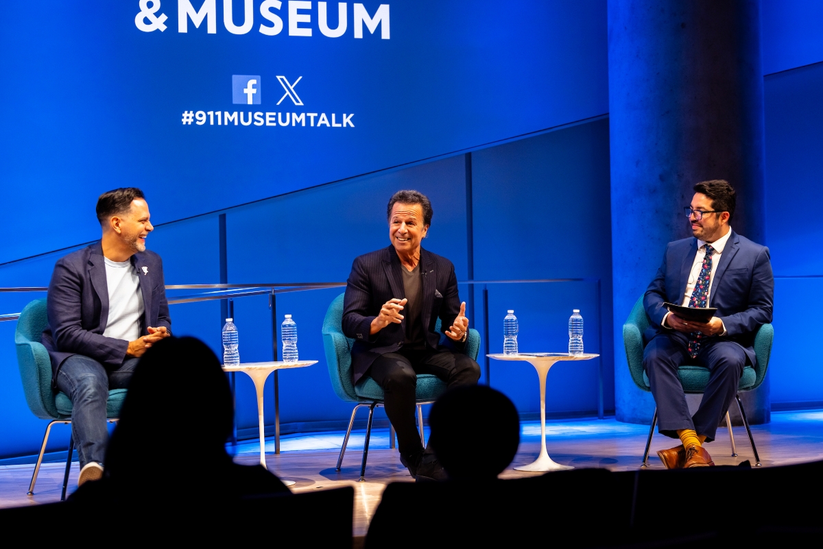 Three men sit on stage in front of a blue screen