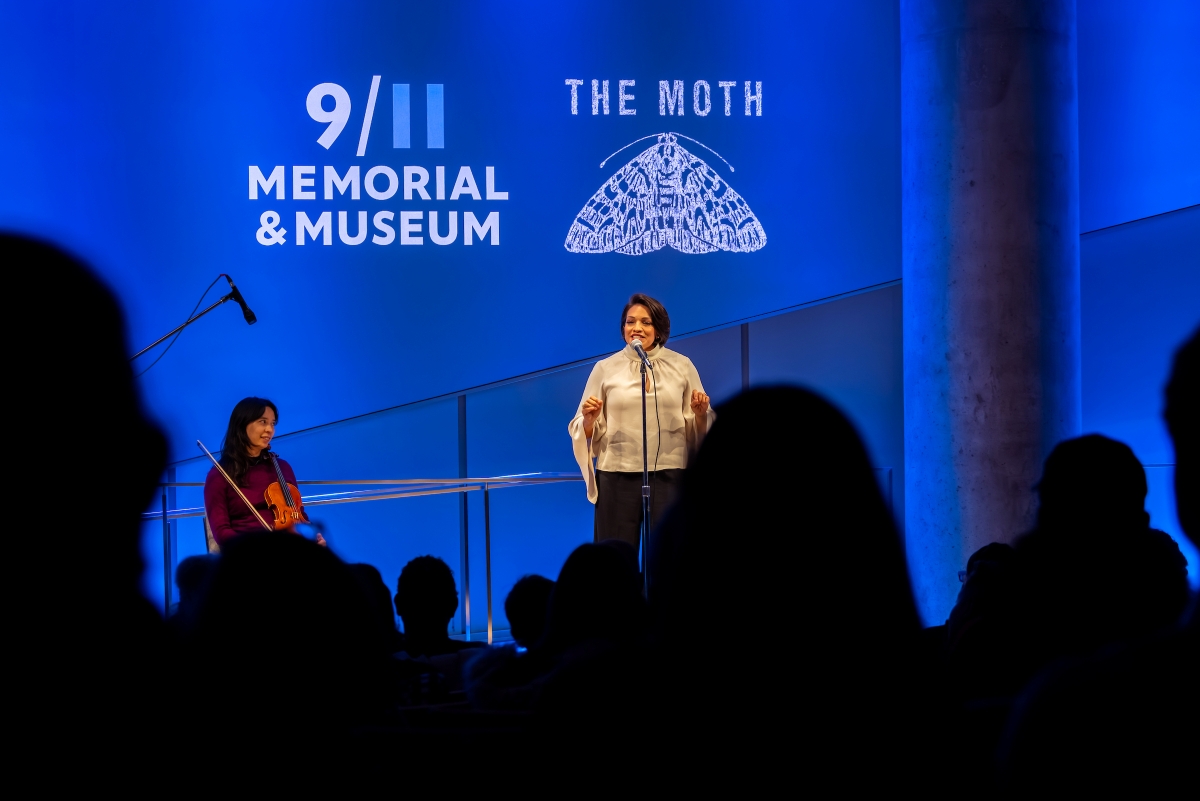 view from the back of the audience, heads visible, speaker and violinist visible
