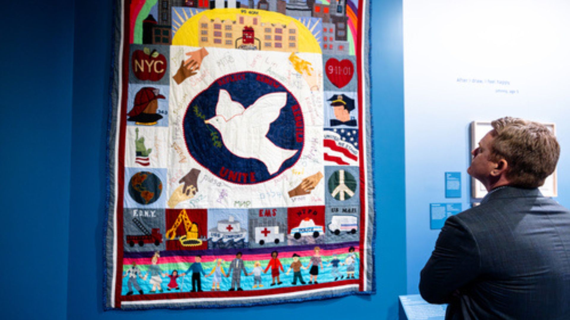 A man looks at a commemorative quilt hanging on a gallery wall.