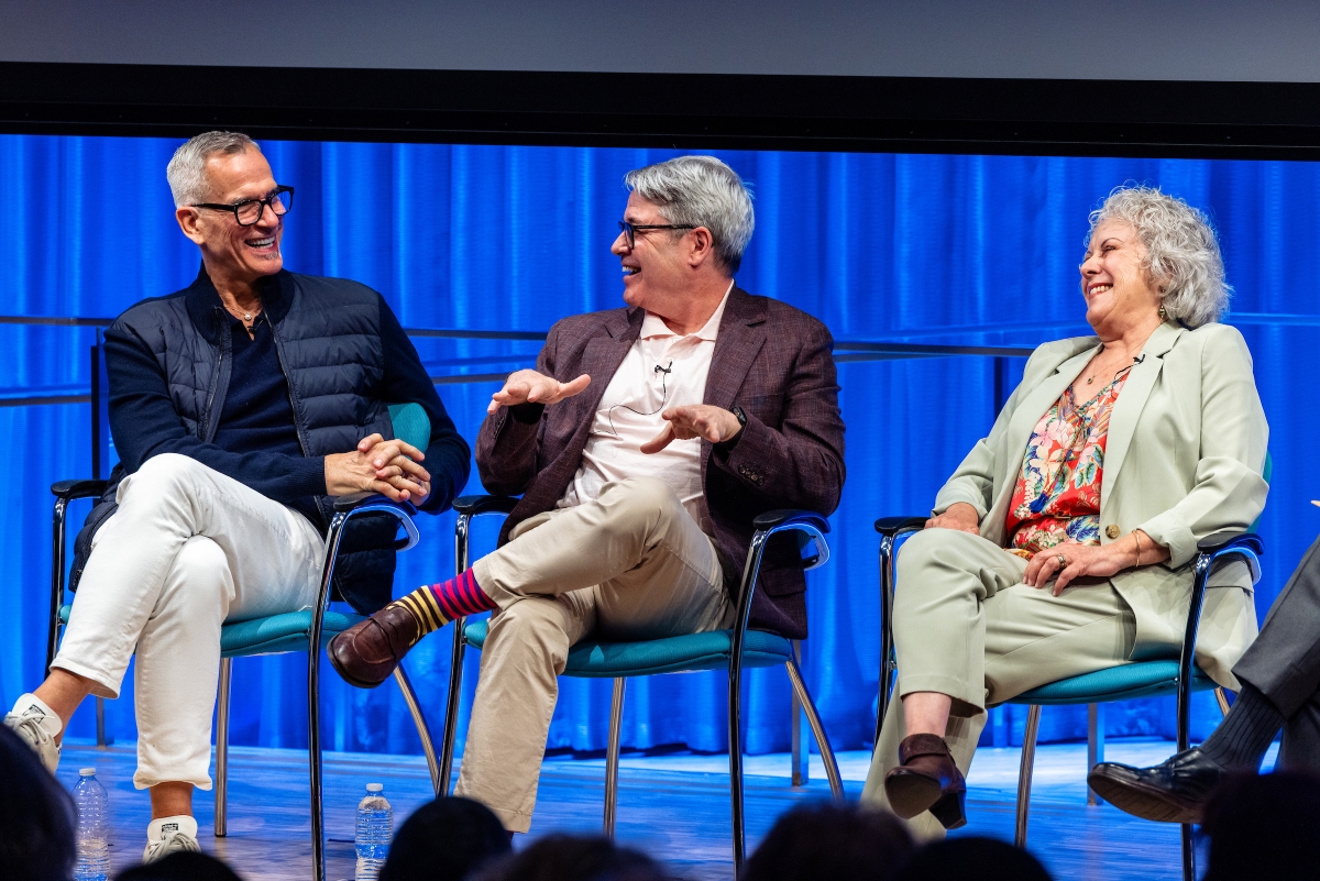 Three people smile and laugh on stage