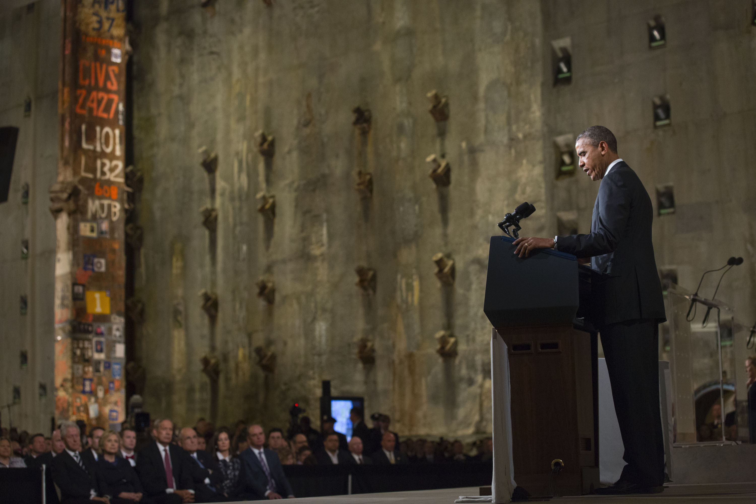 President Barack Obama speaks in Foundation Hall at the dedication of the 9/11 Memorial Museum on May 15, 2014. Former President Bill Clinton, Secretary of State Hillary Clinton, former New York Governor George Pataki, former Mayor Rudy Giuliani, and others watch on with the Last Column and slurry wall behind them. 