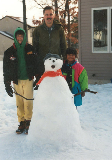 Michael Diehl stands beside a snowman with his son and daughter on a snowy day. 