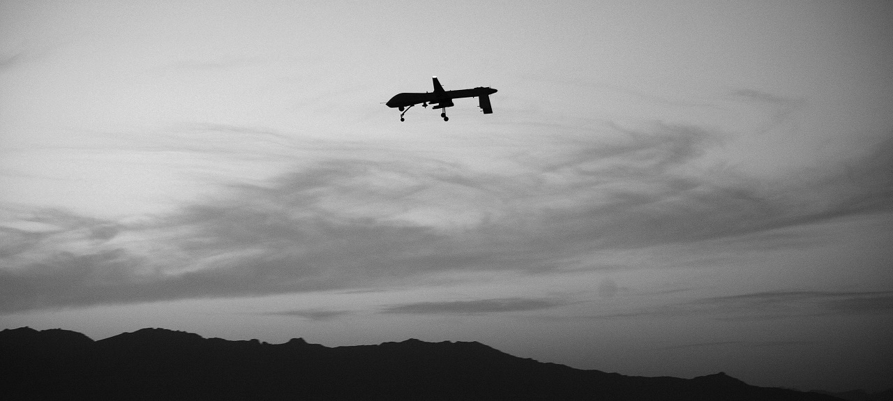 Silhouetted image of a drone in the sky flying over mountain tops. 