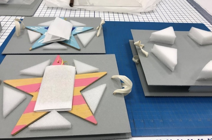 Multicolored wooden stars rest on gray cardboard waiting to be packaged. 