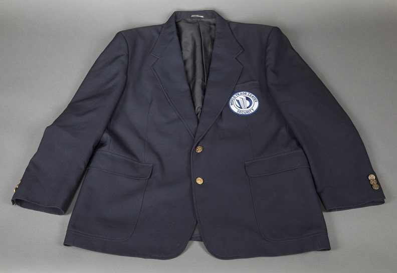Navy blue blazer with brass button and an indiscernible circular white and blue patch sewn on left pocket. 