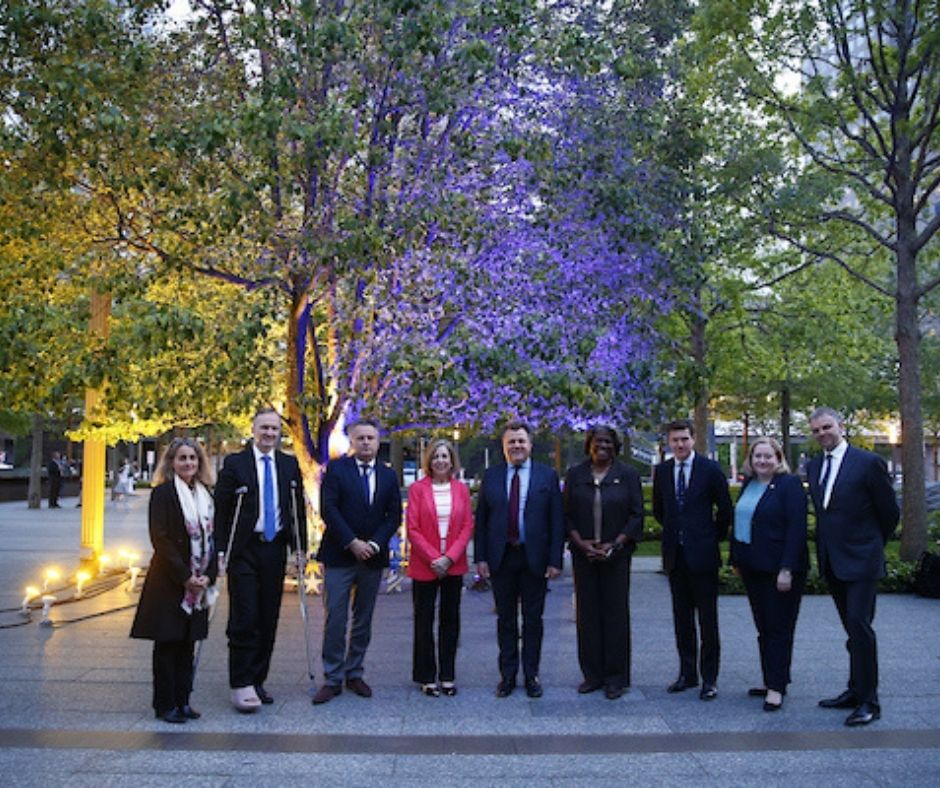 A group of nine people - four women and five men - pose on the plaza 