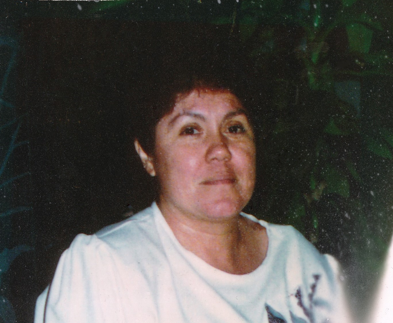 A woman in a white t-shirt, with short, dark hair, looks at the camera 