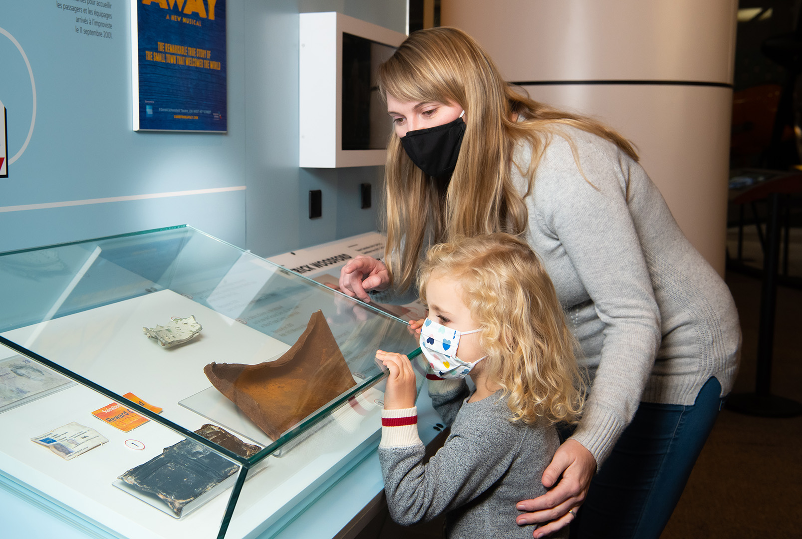 An adult and a child gaze at a glassed case containing artifacts including small, frayed books. 