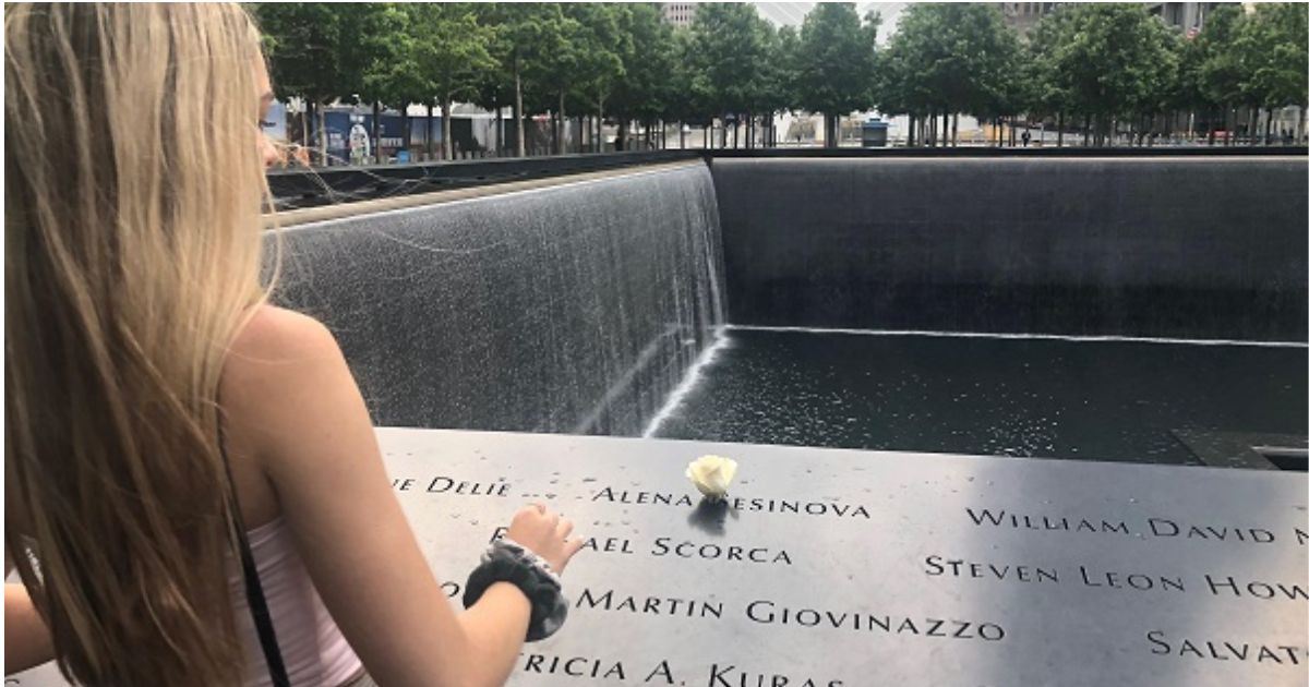 The back of a young woman with long blonde hair placing a rose at a name on the Memorial 