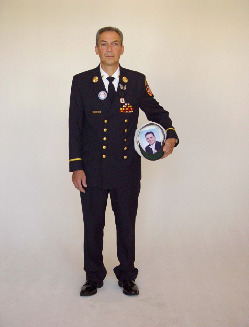 A man stands in FDNY dress uniform in front of a white background.