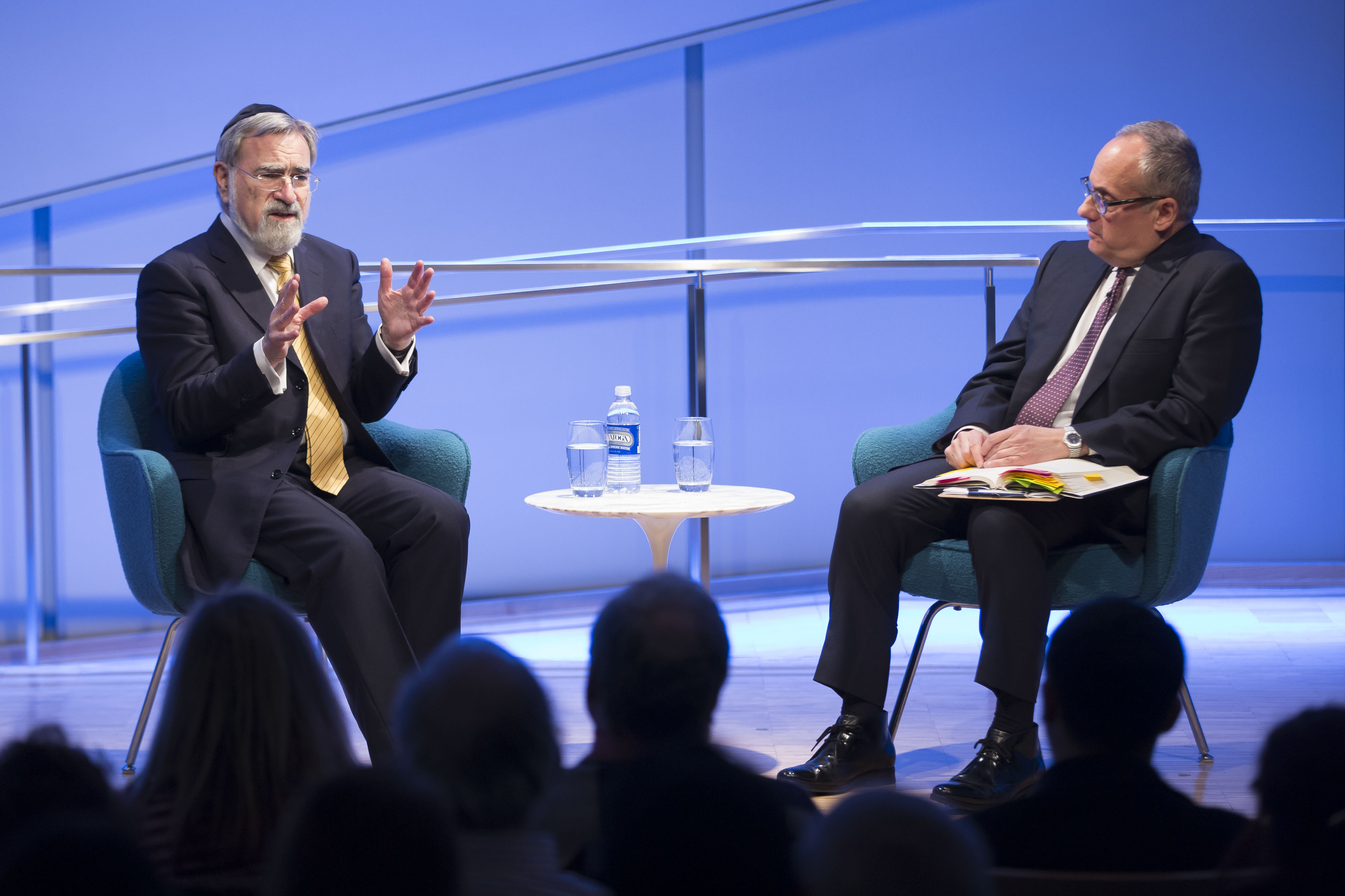 In this wide-angle shot, which shows audience members at the 9/11 Memorial Museum auditorium in in silhouette in the foreground,  the Rabbi Jonathan Sacks, who had retired as chief rabbi of the United Hebrew Congregations of the British Commonwealth when he visited in 2016, raises both his hands as he gestures in conversation with Cliff Chanin.