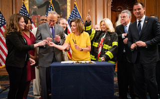 With a row of American flags in the background, a group of men and women pass a pen around as they prepare to sign a document