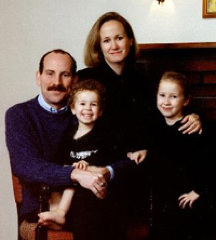 Two adults - a mustached man and a light brown-haired woman pose with two small girls on their laps