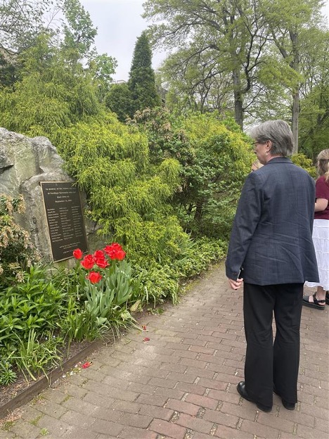 Elizabeth Hillman reads a plaque mounted on a rock in a lush garden.