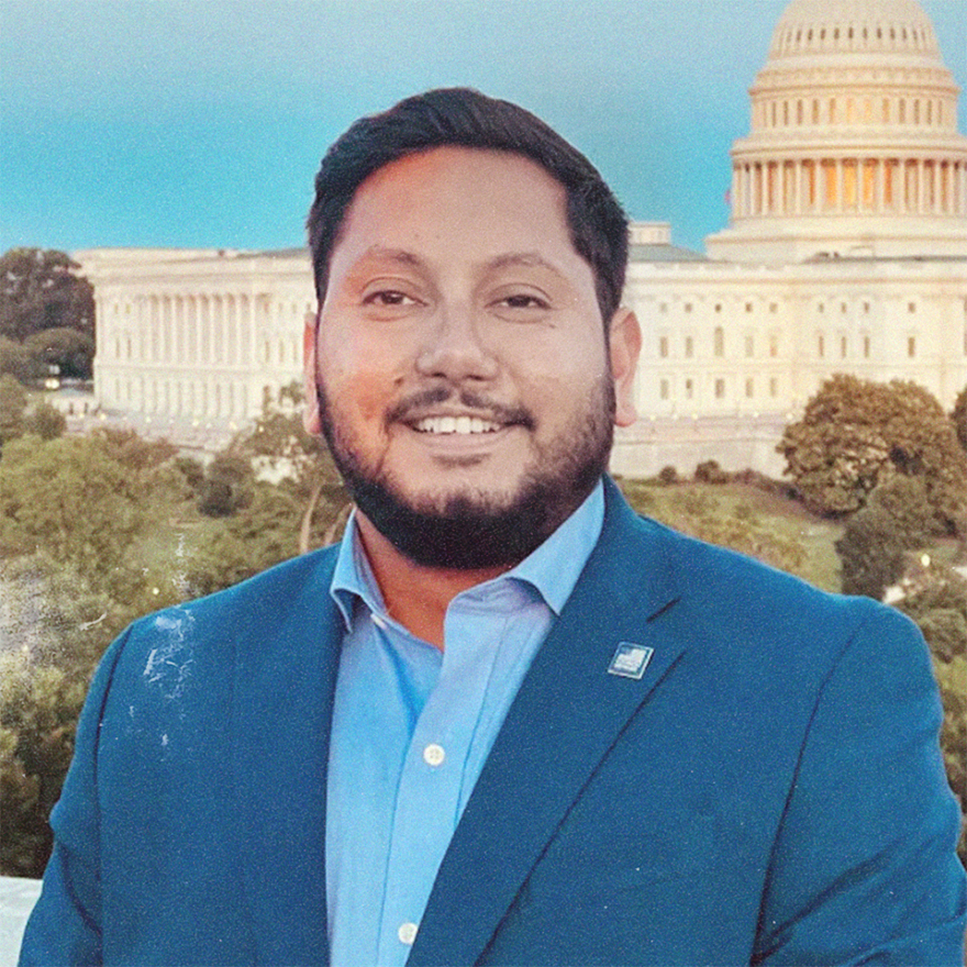 Naveed Shah, wearing a blue suit, posed in front of US Capitol Building