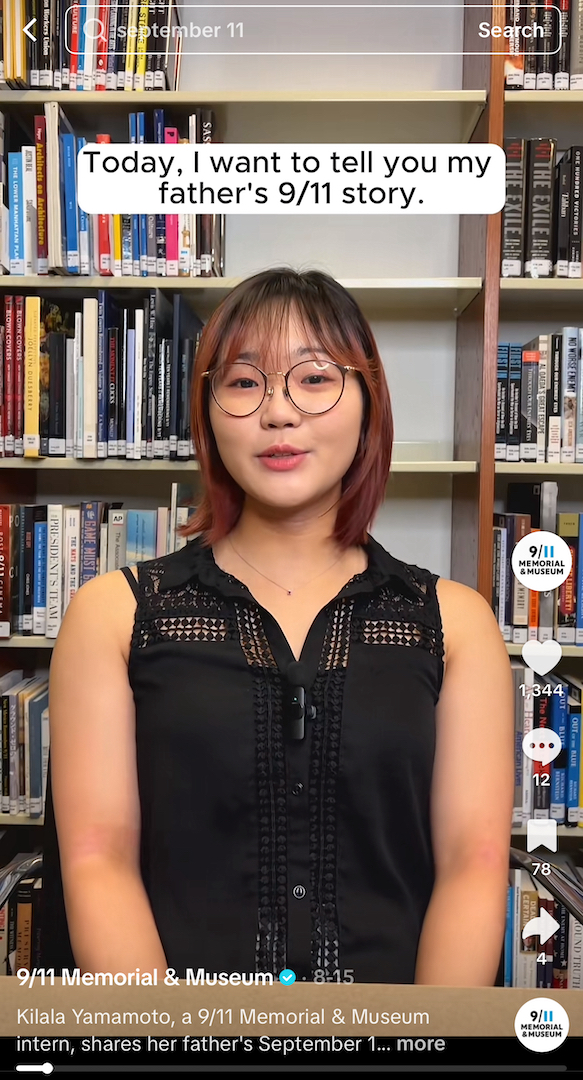 Kilala Yamamoto, wearing glasses and a black top, stands in front of bookcases.