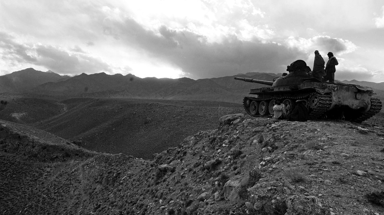 Two individuals standing on a tank overlooking a rocky desert landscape.