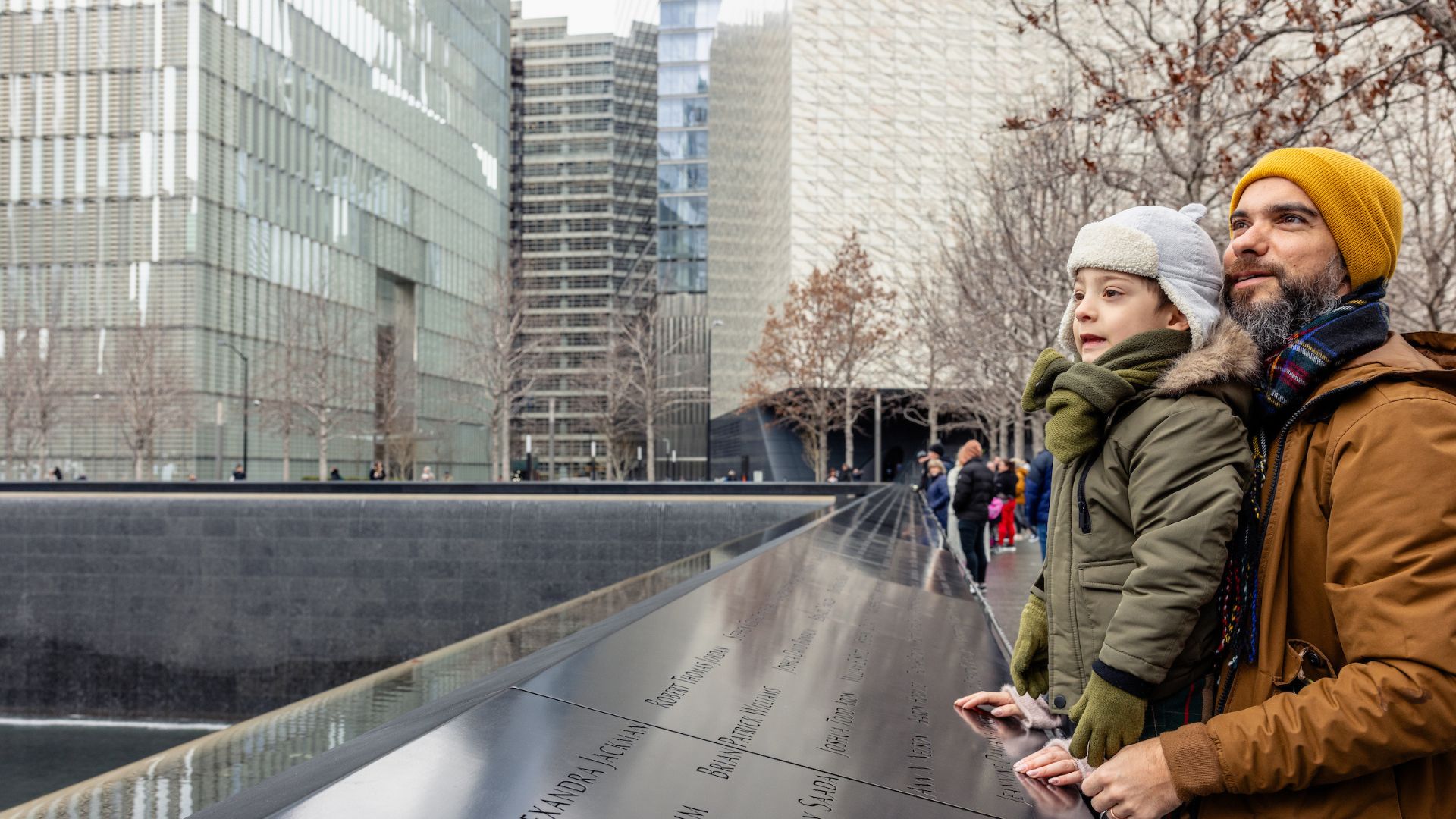 An adult and a child, both in winter coats, look out onto the Memorial pool.