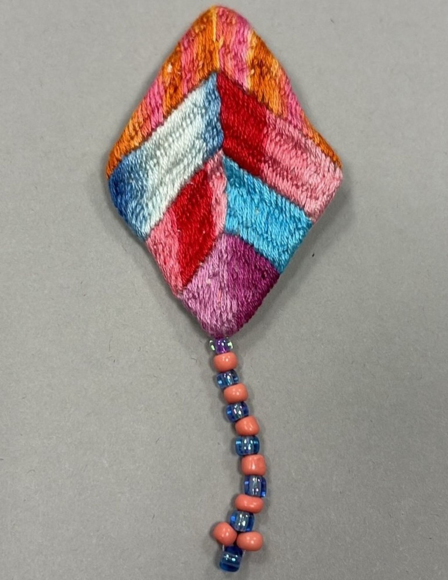 A multi-colored hand-sewn kite pin