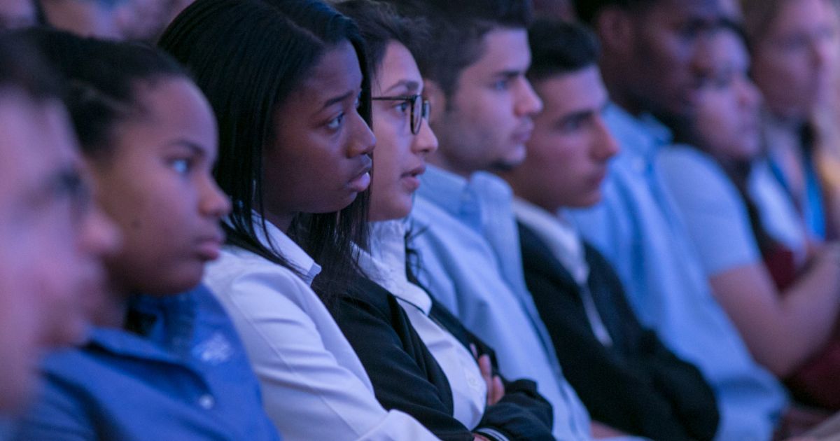 Students seated in an audience, listening attentively to a presentation.