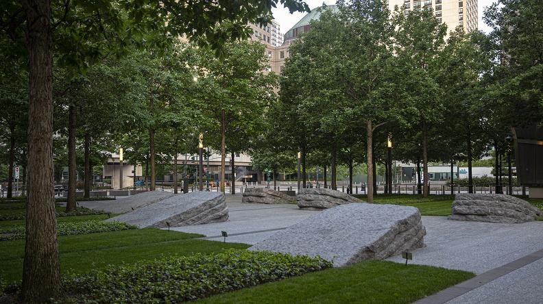 It’s just after dawn at the Memorial Glade. About a dozen oak trees cast a shadowy green over a shaded path and six stone monoliths. The area is quiet and no one is in sight. Ivy beds and fresh-cut grass flank the path, which turns to a building beyond the trees.