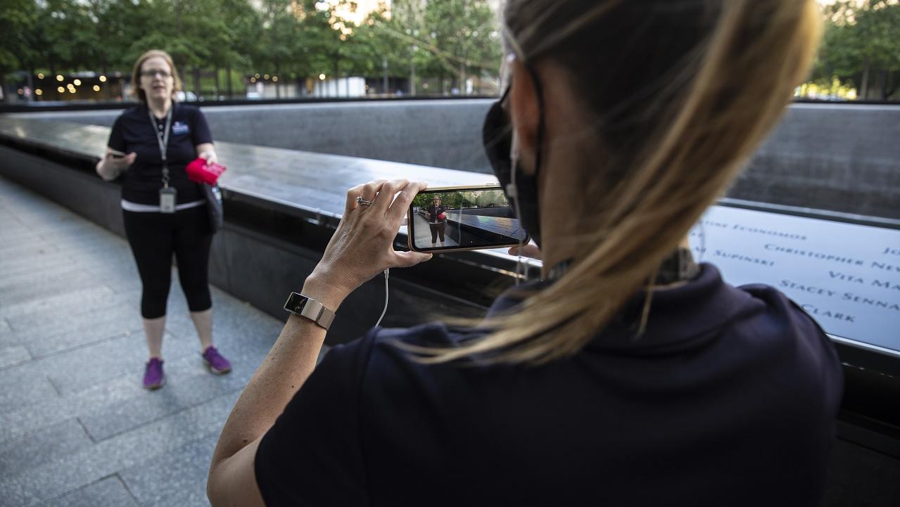 A woman uses a smartphone to film another woman addressing the camera at the 9/11 Memorial.