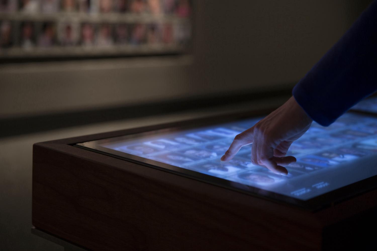 Hand with finger extended and touching a digital screen emitting a blue light 