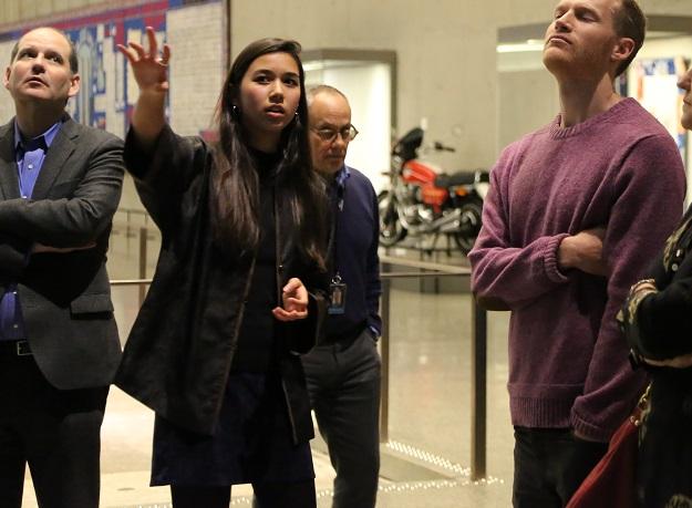Annalee Tai, a 9/11 Museum ambassador, leads a tour at the Museum. Several visitors stand beside her as she points towards something out of view.