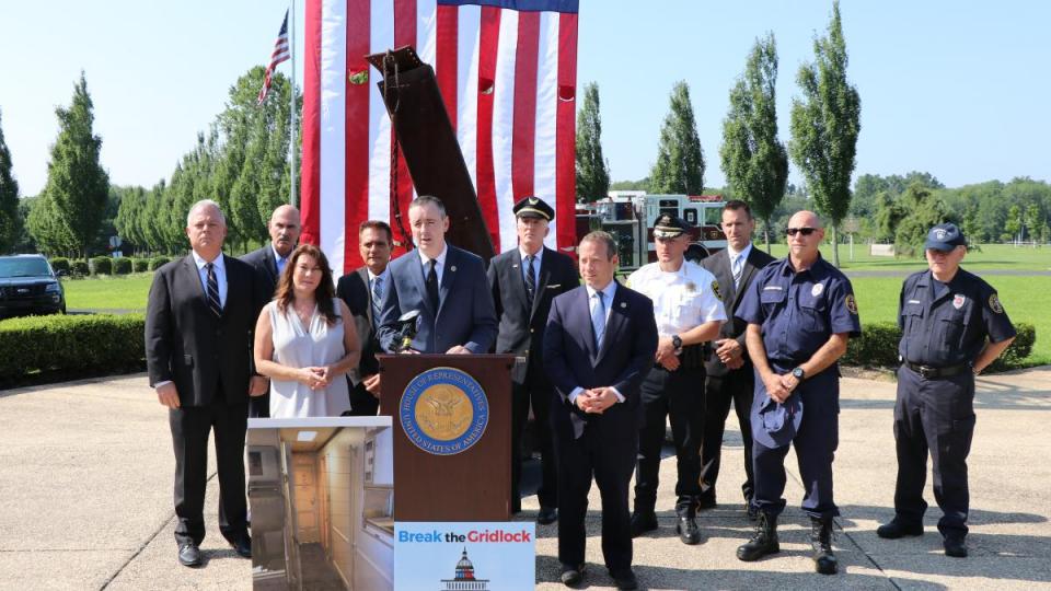 Congressmen Brian Fitzpatrick and Josh Gottheimer stand with Ellen Saracini during an event on a sunny day at the Garden of Reflection 9/11 Memorial in Bucks County, Pennsylvania.