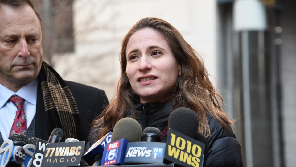 A young woman speaks into a group of microphones from assorted media channels during a press conference.