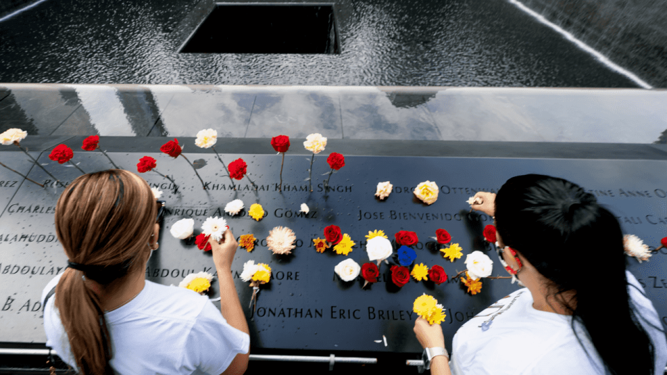 An overhead angle shows two young women, dressed in white, placing flowers on the bronze names panels of the 9/11 Memorial on the 19th Anniversary of the 2001 attack.