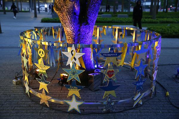 Metal railing at base of tree trunk, with hand-painted wooden stars hanging from it 